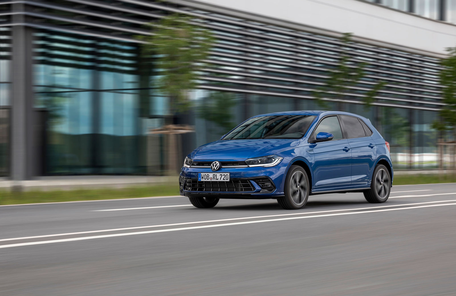 Blue Volkswagen Polo driving past a modern building